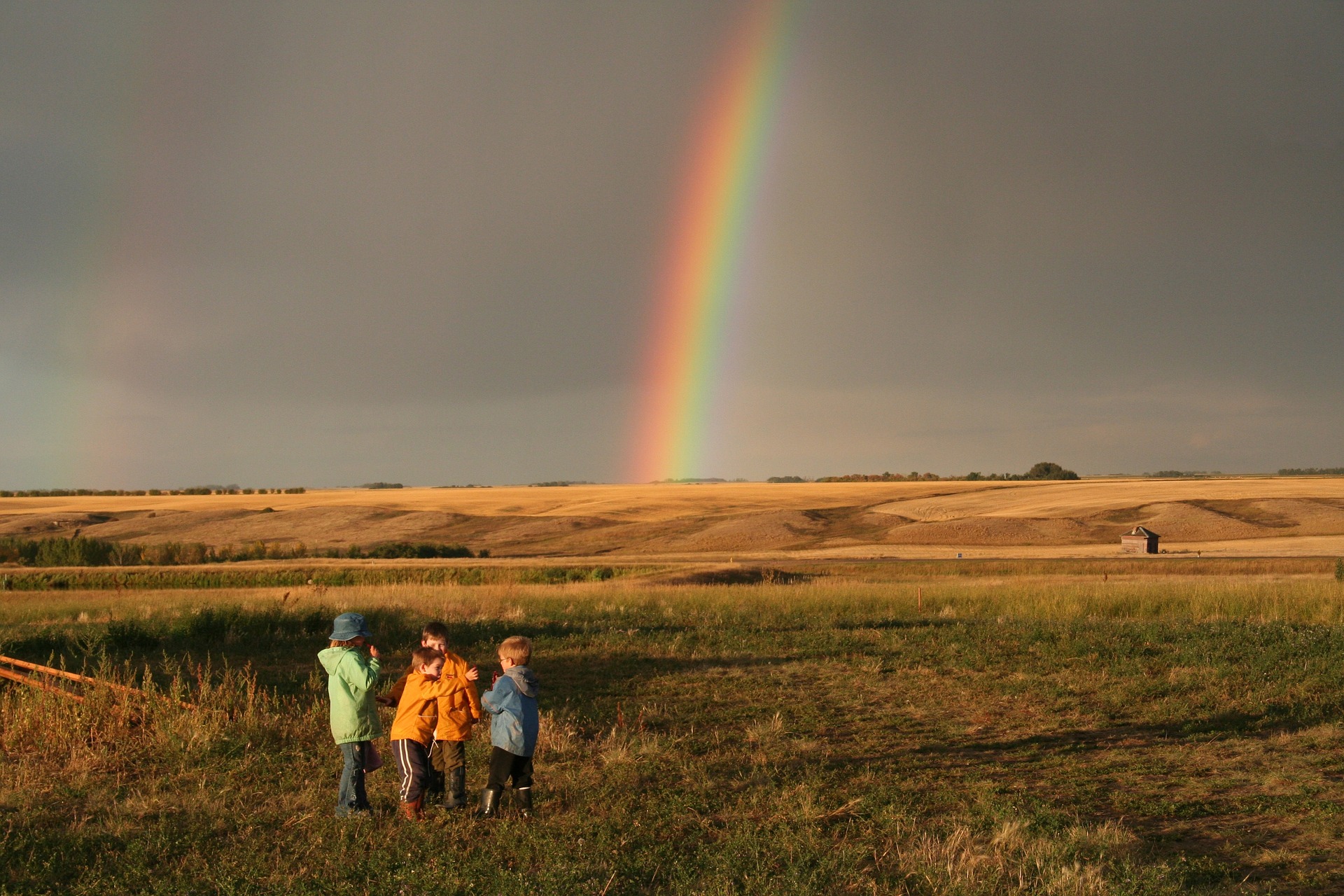 se mira un paisaje con un grupo de niños quienes observan un arcoirirs en el horizonte.