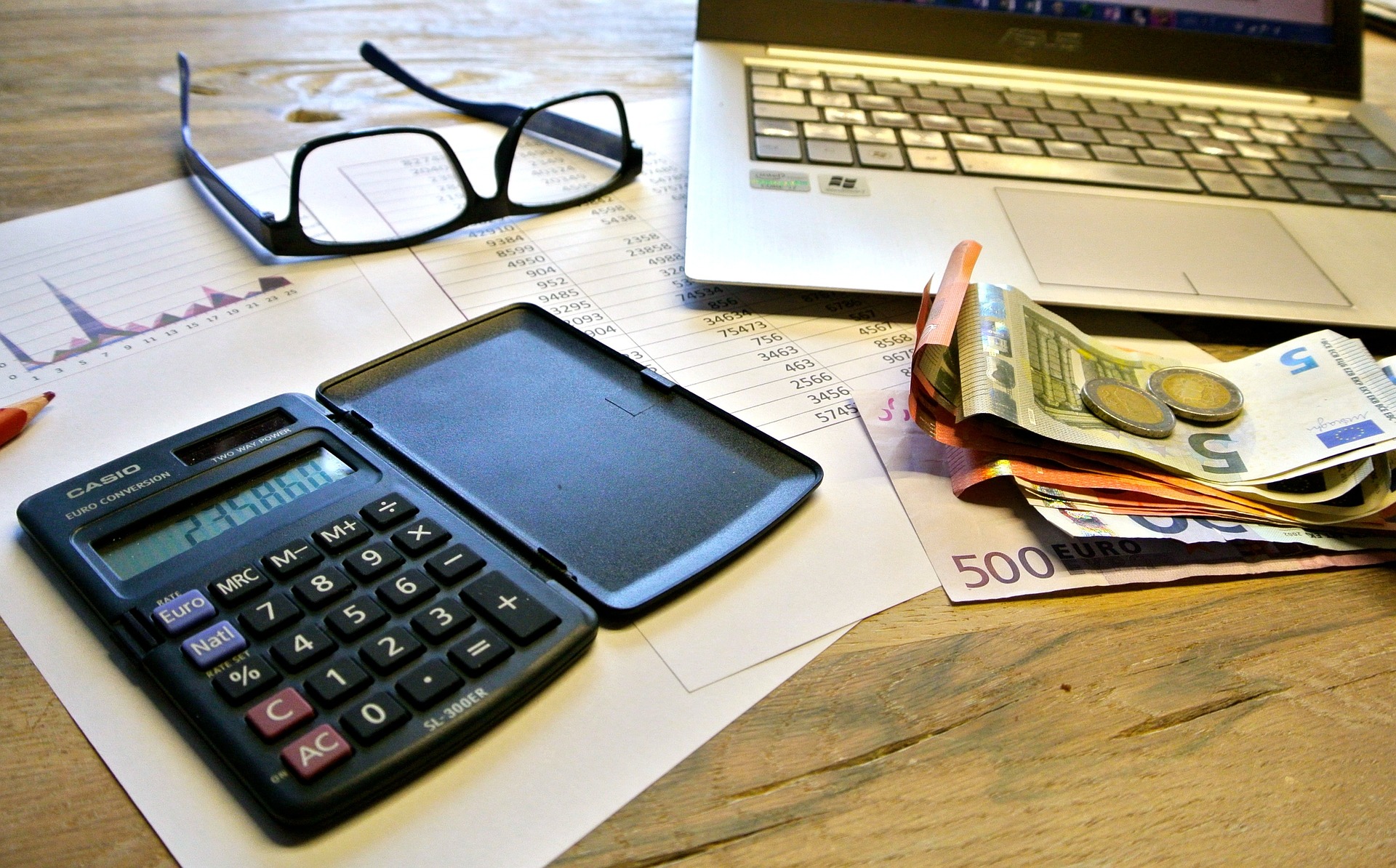 Laptop, dinero, calculadora y lentes sobre una mesa.