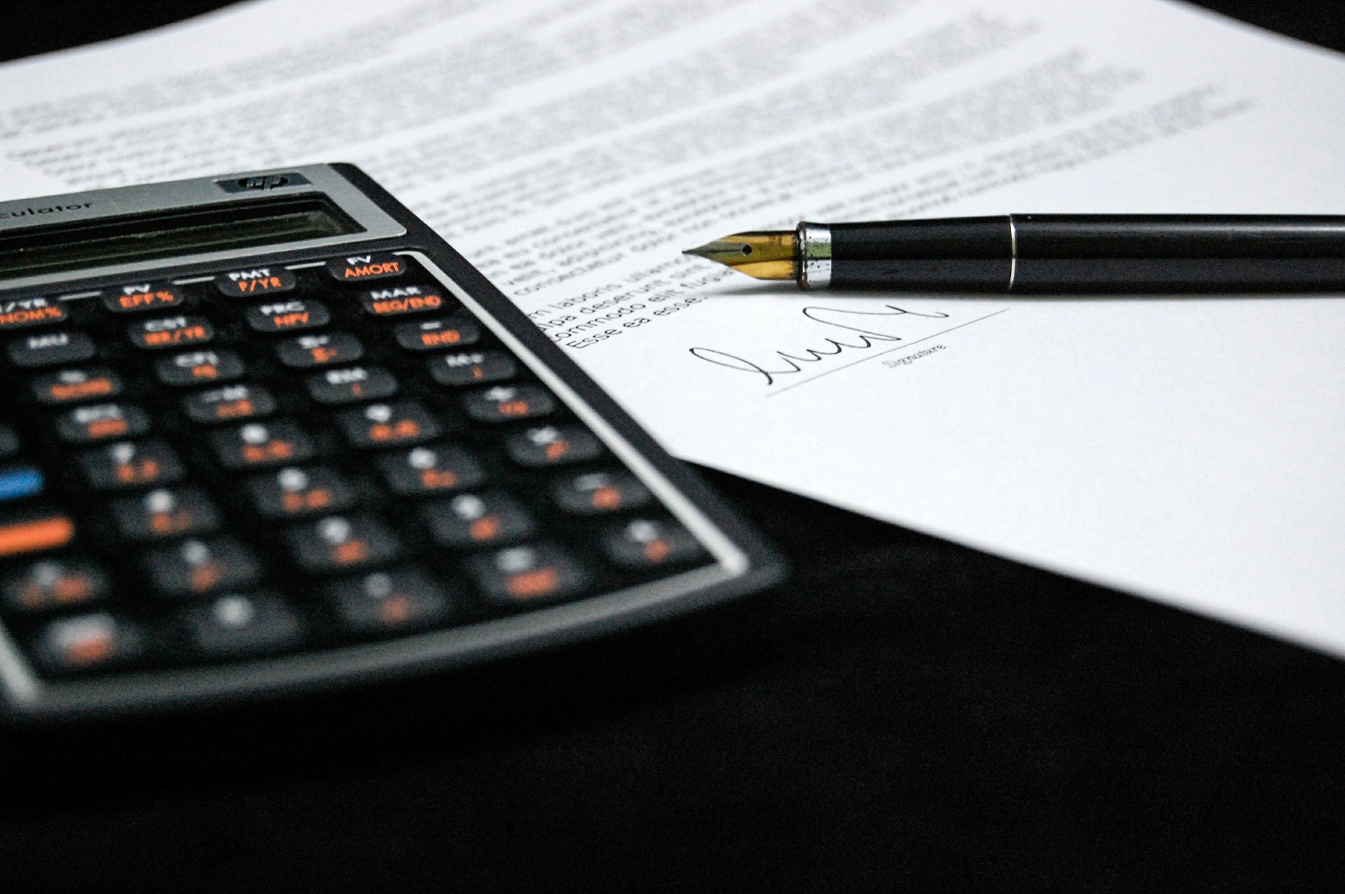calculadora, documento y pluma fuente sobre una mesa.