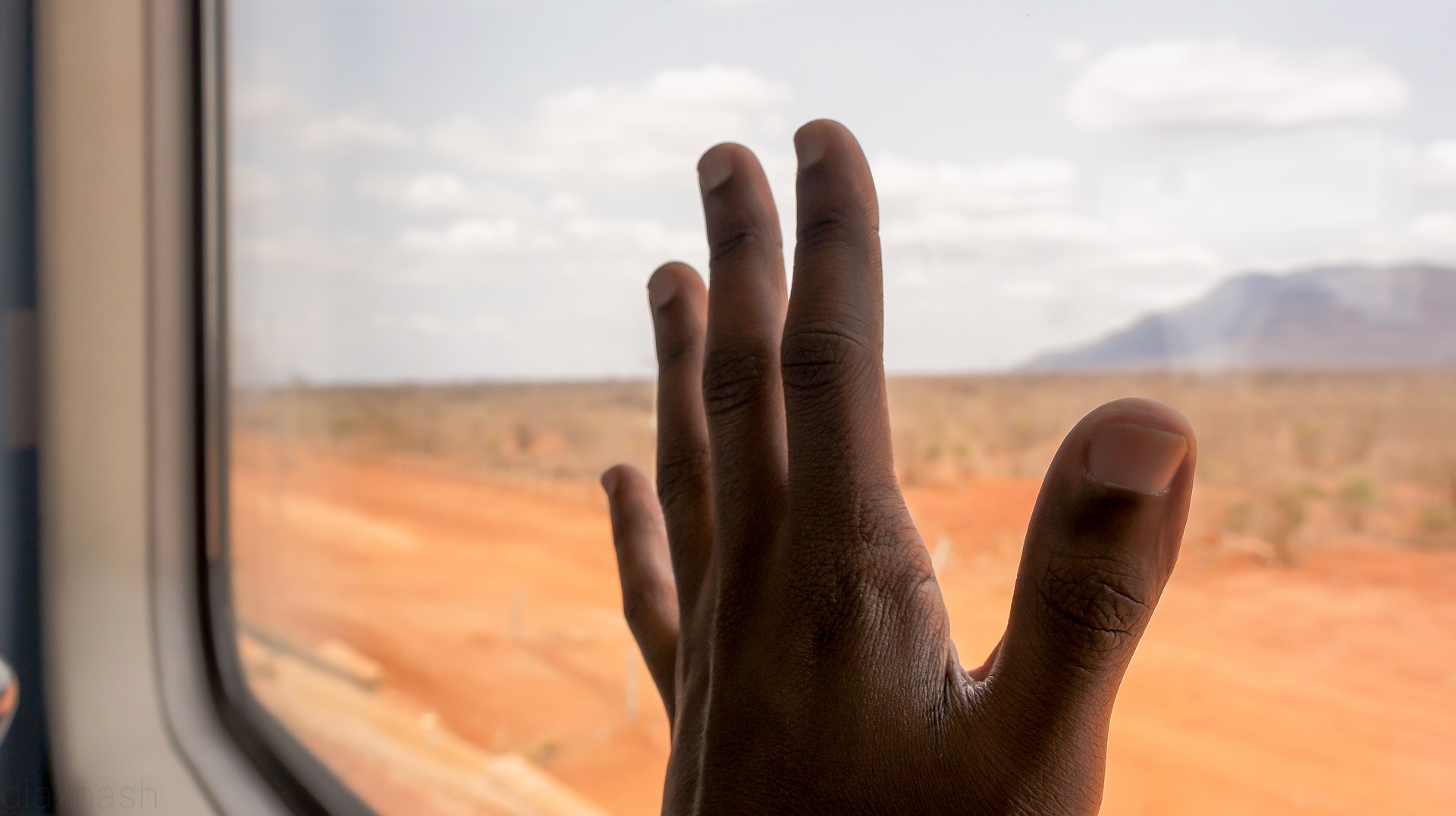 Una mano toca el vidrio de la ventana de un tren; al fondo se oberva un paisaje.