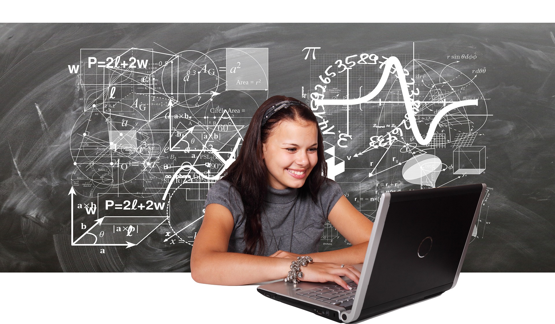 Una mujer joven mira sonriente su computadora y, de fonodo, hay un pizarrón negro con fórmulas matemáticas escritas con gis blanco. 